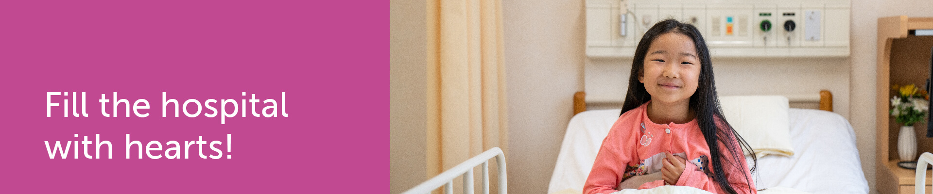 Fill the hospital with hearts! A patient with long dark hair and wearing a pink top smiles while sitting in a hospital bed.